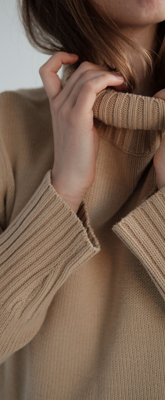 Hands adjusting a beige knitted turtleneck sweater
