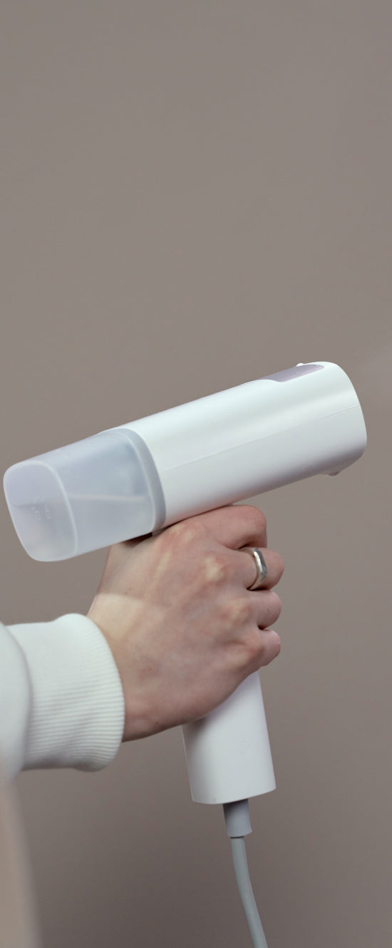 Hand holding a white handheld steamer against a neutral background