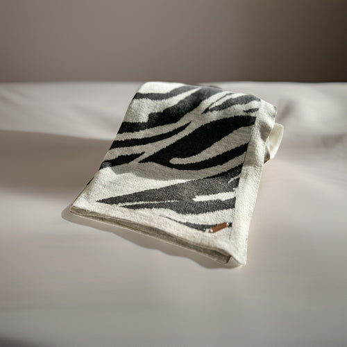 A folded luxury travel blanket with a zebra-like pattern in black and white, placed on a bed.